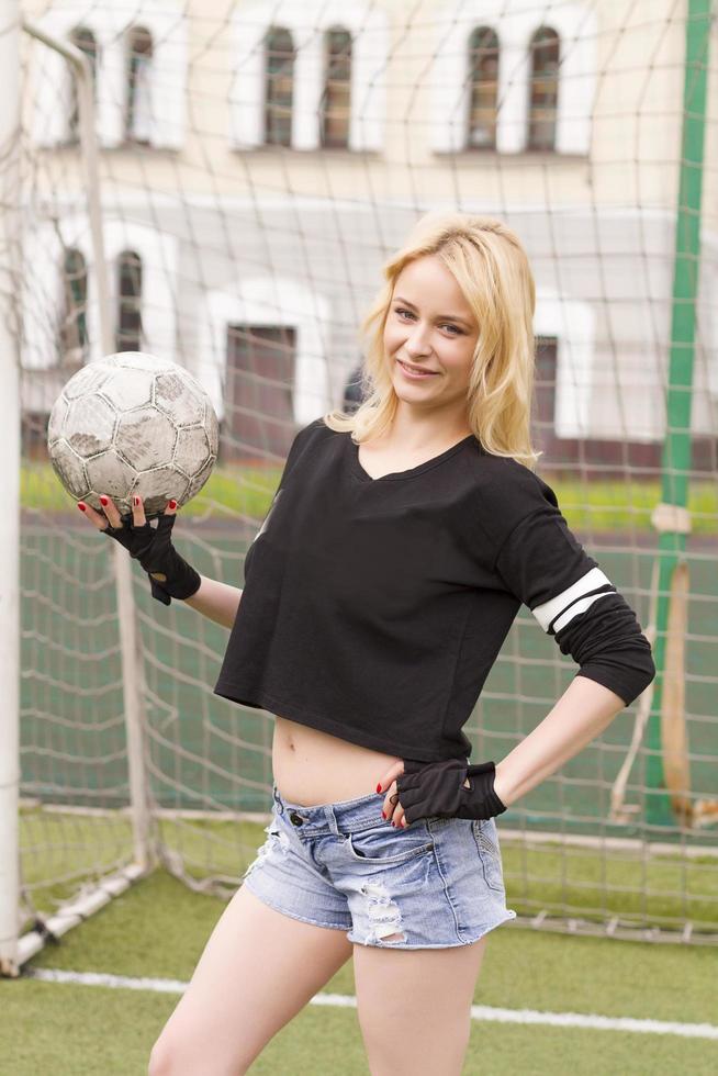 linda loira com uma bola no gol de futebol. foto