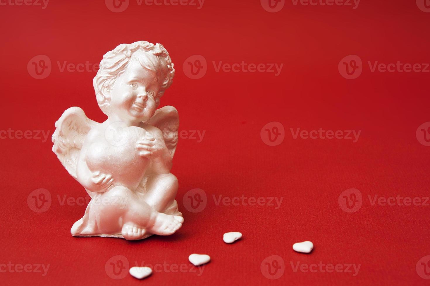 anjo de gesso closeup com coração em um fundo vermelho. cupido decorativo para dia dos namorados. foto