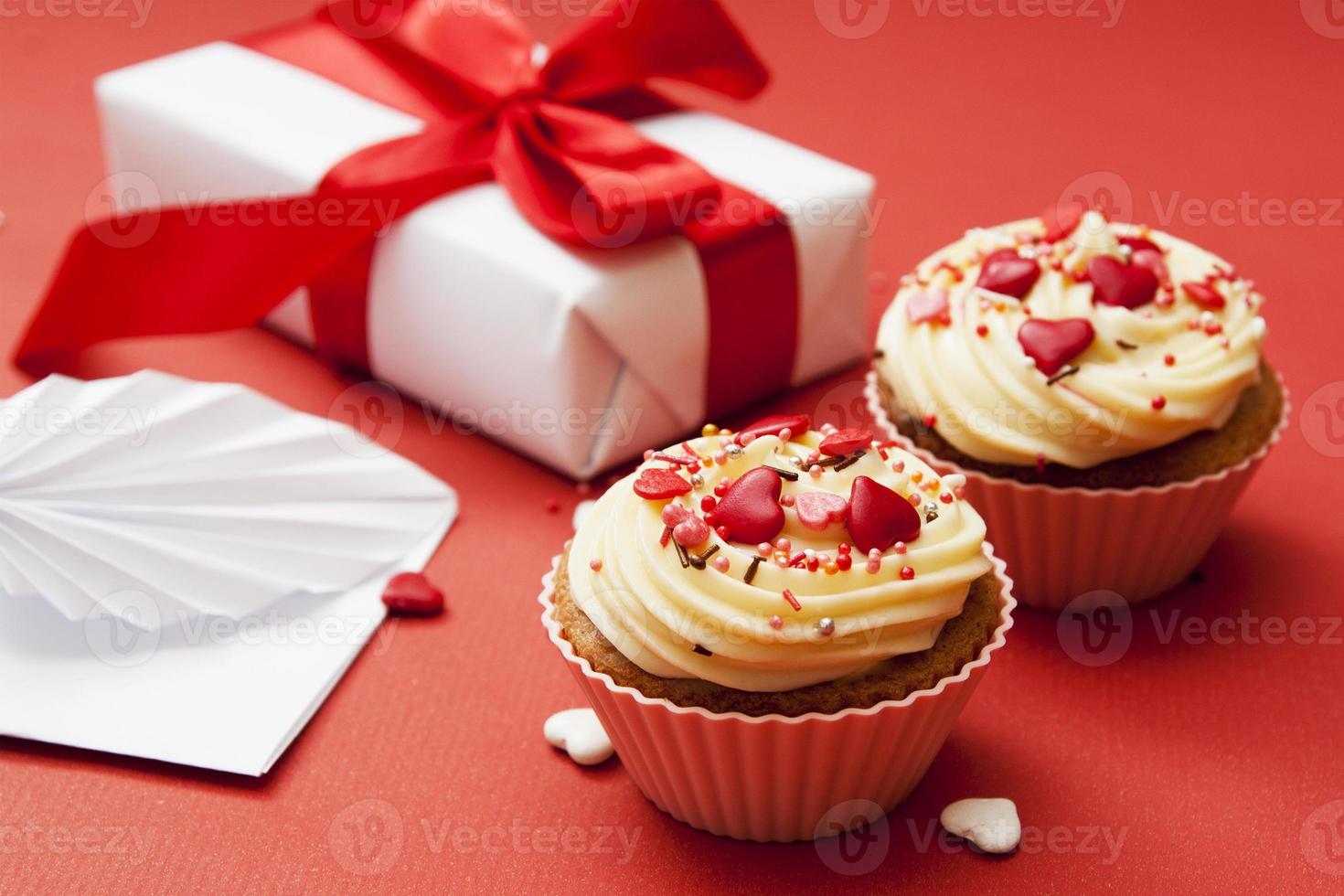 close-up de dois cupcakes com decoração de creme e coração em um fundo vermelho com presente e envelope. foto