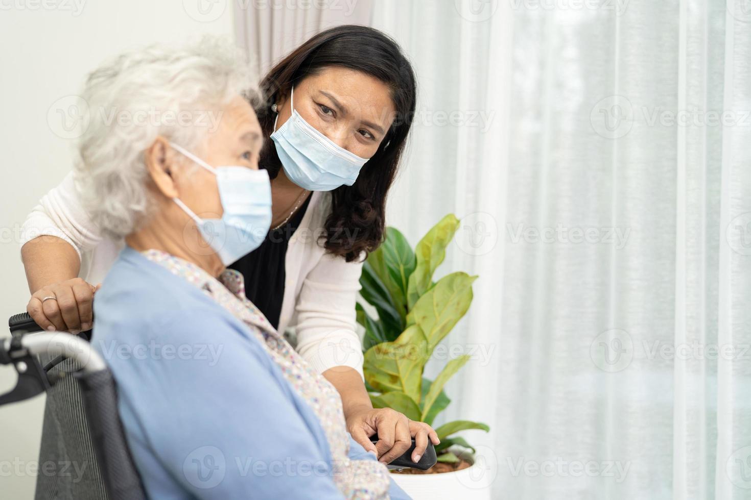 cuidador ajuda idosa asiática ou idosa sentada em uma cadeira de rodas e usando uma máscara facial para proteger a infecção de segurança do coronavírus covid-19. foto