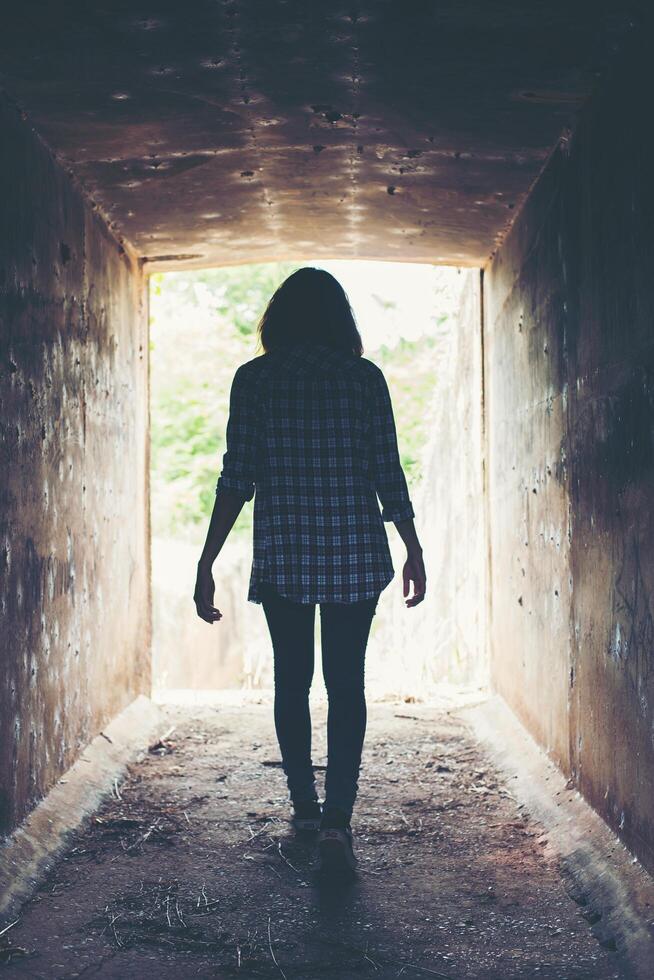 silhueta de mulher hipster andar no túnel. luz no fim do túnel foto