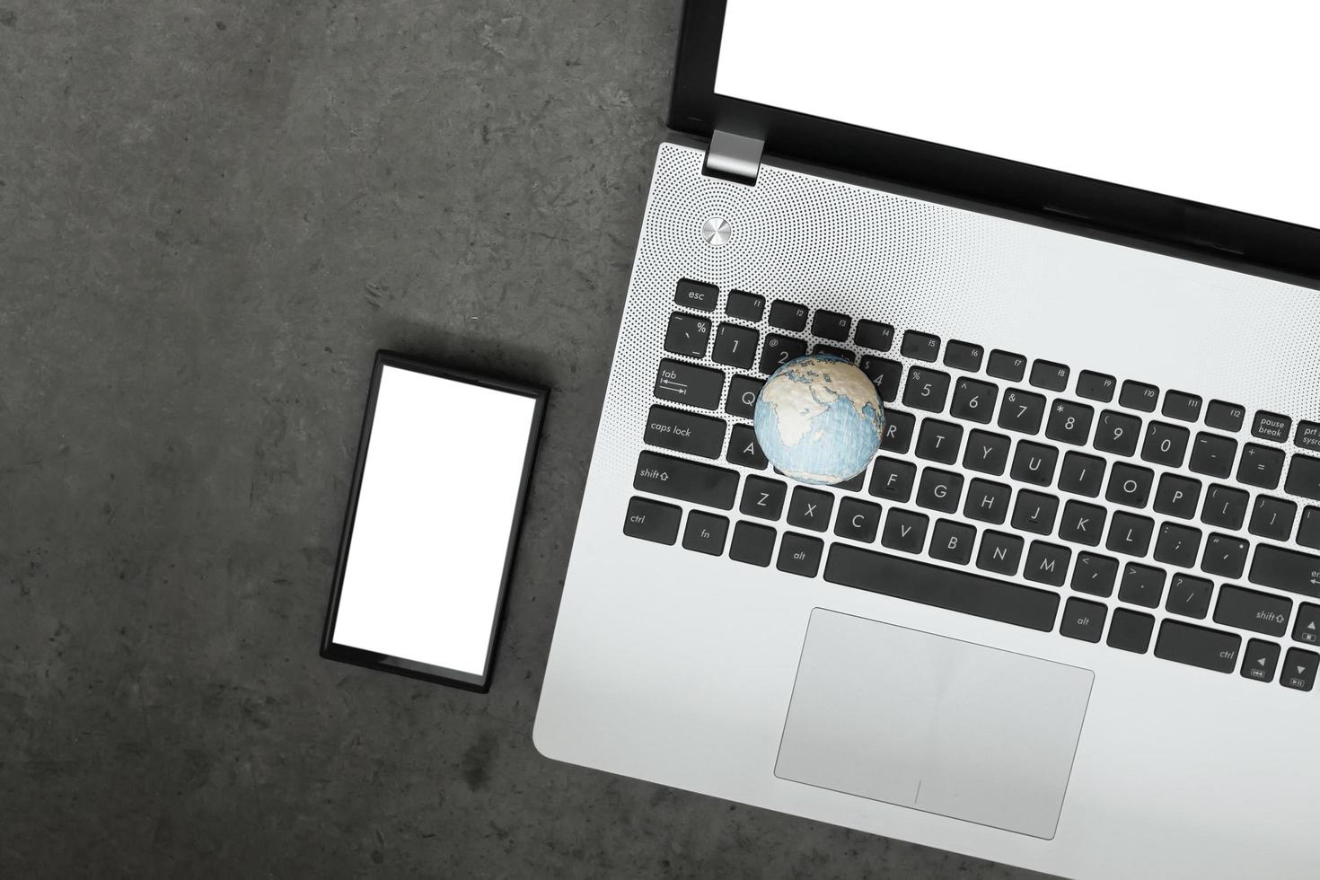 globo de textura desenhado à mão com computador portátil de tela em branco e telefone inteligente como conceito de internet no fundo da mesa de textura de cimento foto