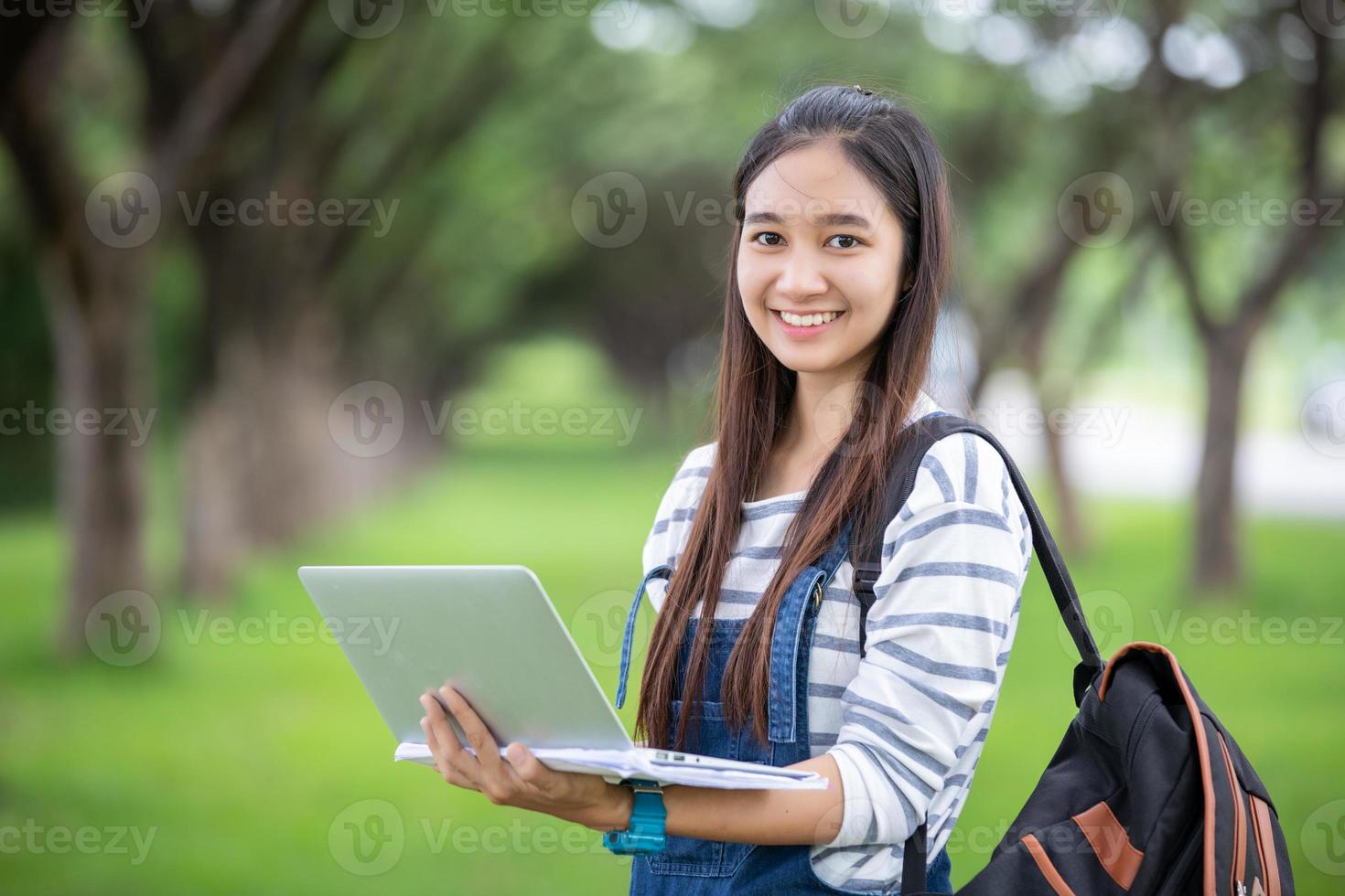 bela estudante asiática segurando livros e sorrindo para a câmera e conceito de aprendizagem e educação no parque no verão para relaxar foto