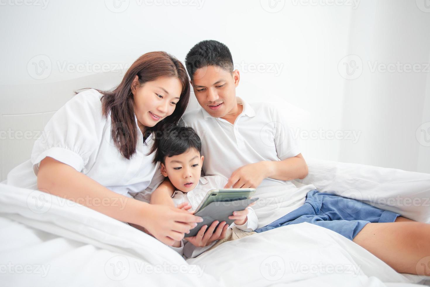 família e filho assistindo e jogando tablet na cama foto