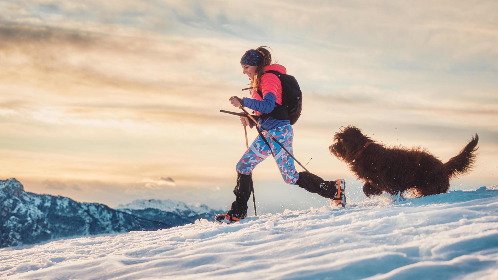 garota esportiva com seu cachorro durante um trekking alpino na neve foto