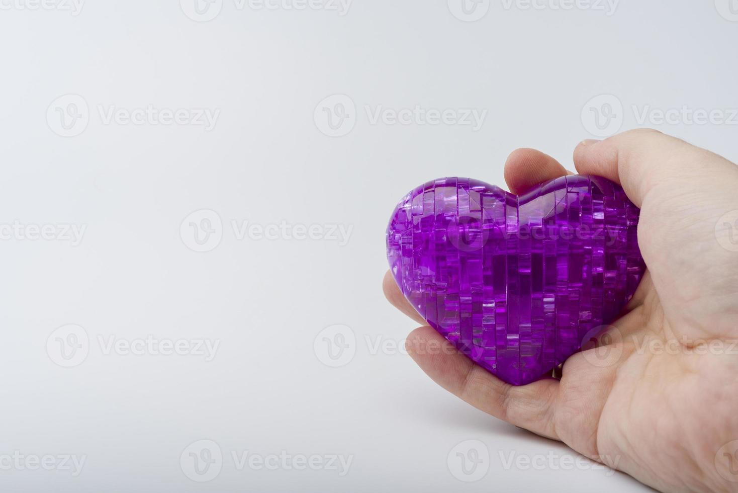 a mão segura o coração em um fundo de plástico branco. foto
