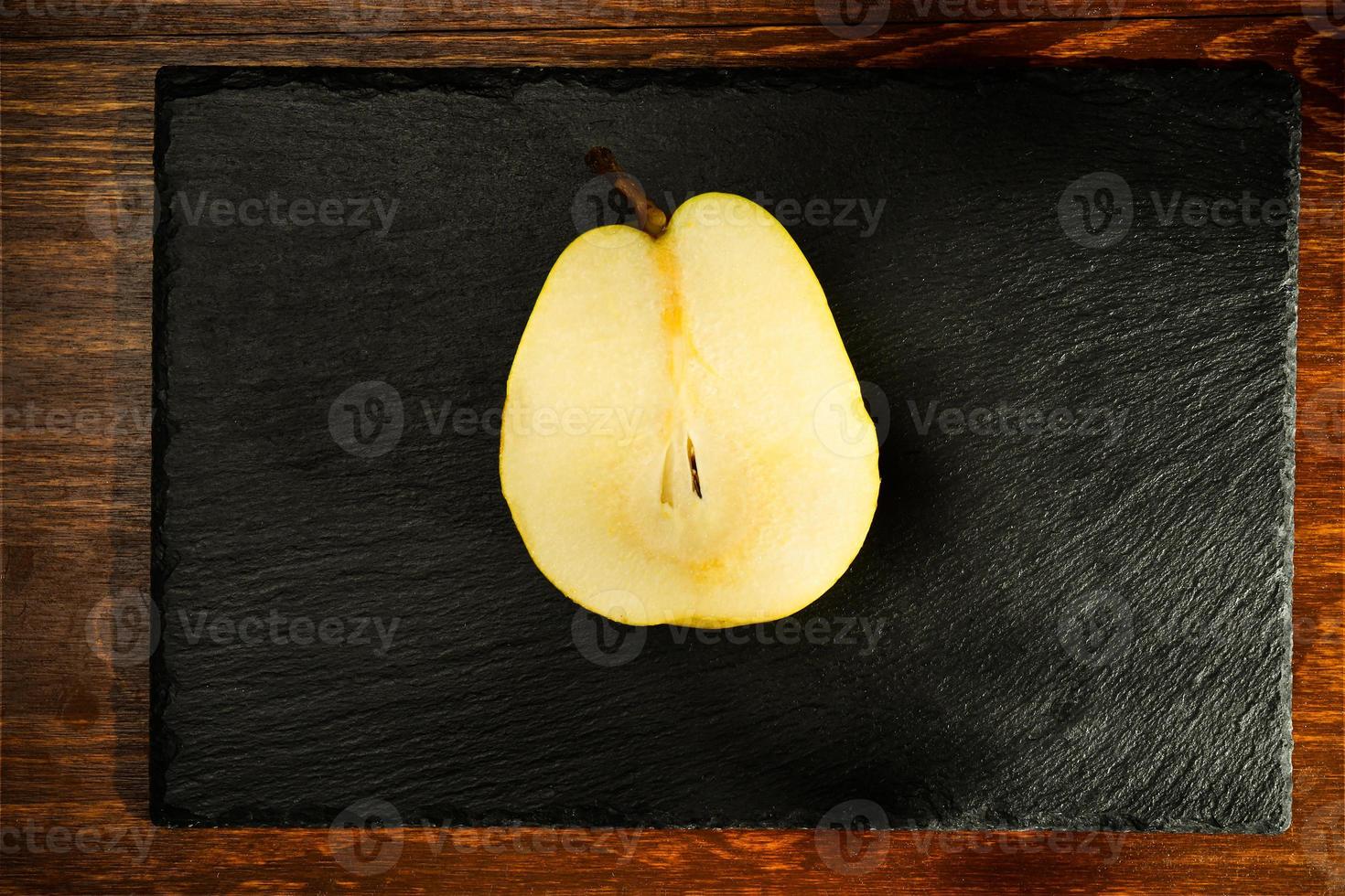 meia pêra amarela natural em uma placa de ardósia, close-up, em uma mesa de madeira, vista superior foto