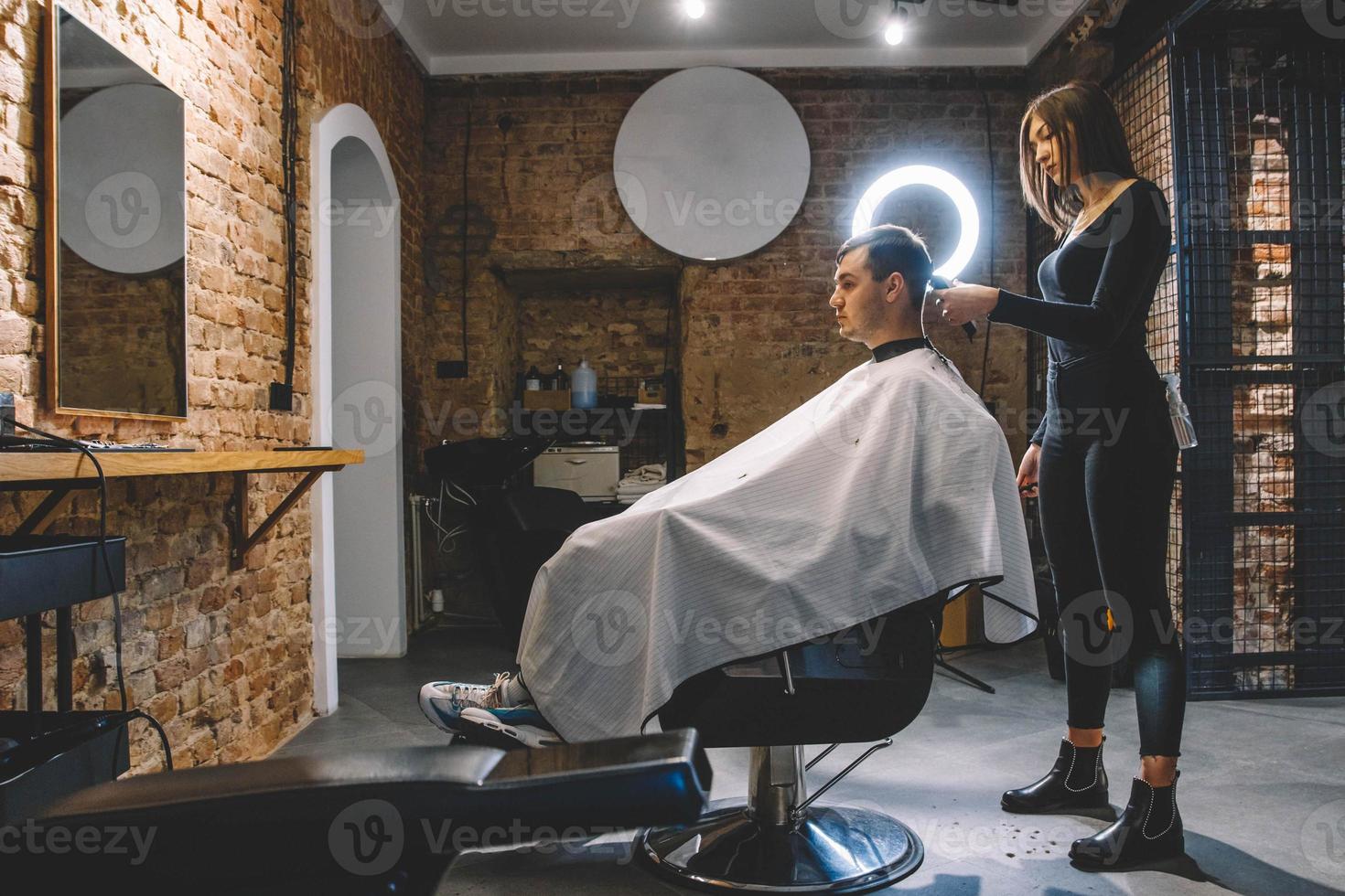 linda cabeleireira cortando o cabelo do cliente com uma tesoura em uma barbearia. conceito de publicidade e cabeleireiro foto