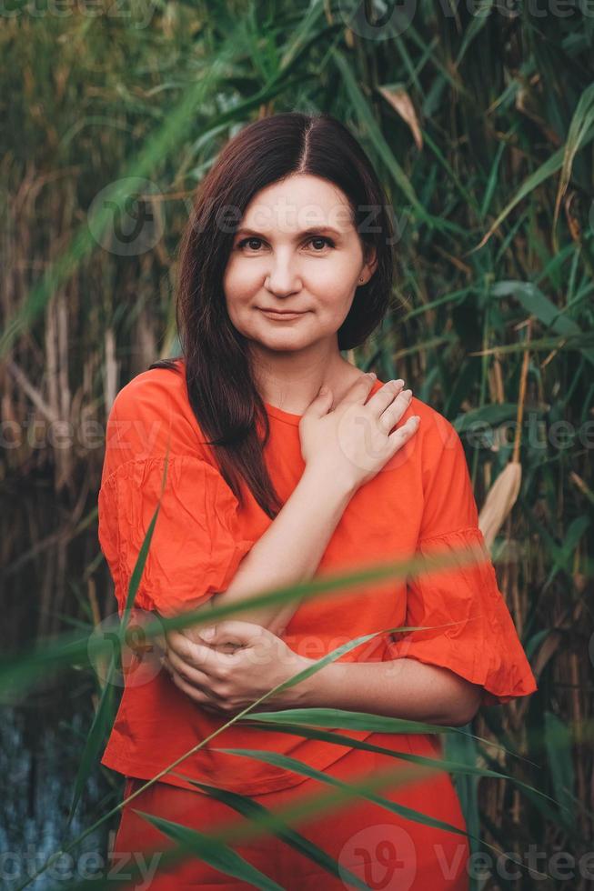 mulher vestida com roupas vermelhas em pé contra o pano de fundo de juncos e lago foto