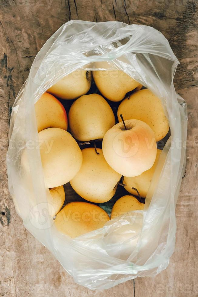 maçãs amarelas em um saco plástico em uma mesa de madeira foto