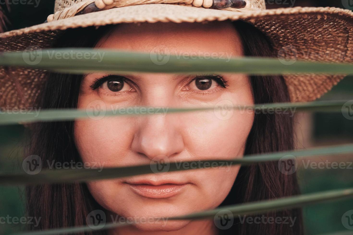 retrato de uma linda mulher com um chapéu de palha olhando para a câmera através das folhas de junco foto