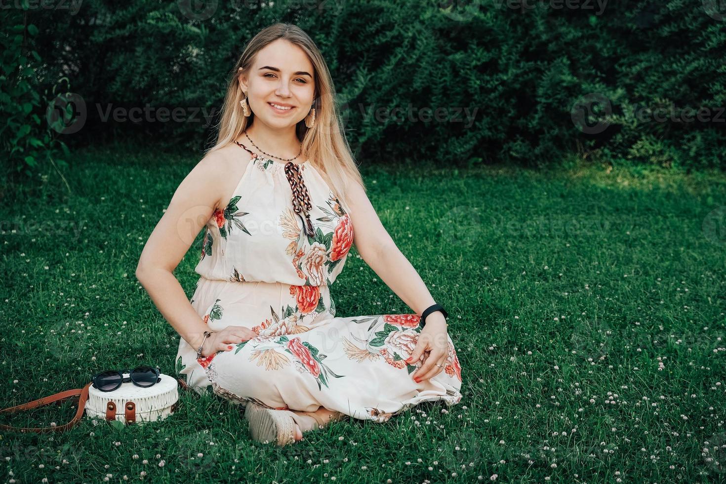 linda mulher loira vestida com vestido de flor, sentado no gramado da grama verde. copiar, espaço vazio para texto foto