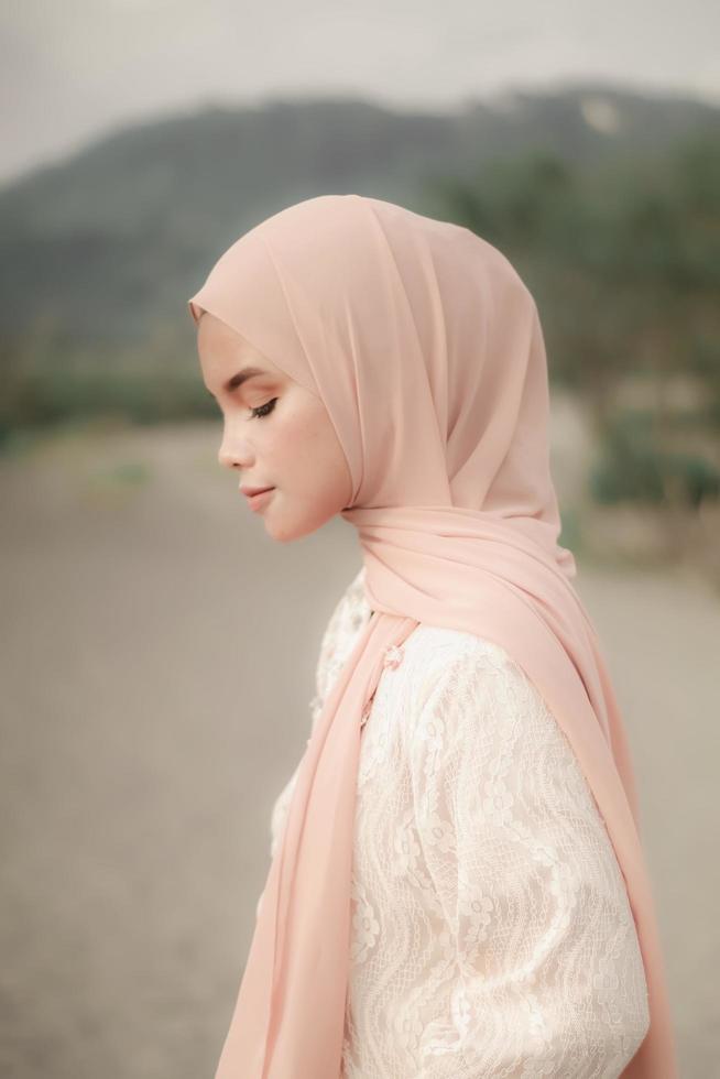 linda modelo feminina islâmica vestindo moda hijab, um vestido de noiva moderno para mulher muçulmana caminha pela areia e pelo mar. um modelo de menina asiática usando hijab se divertindo na praia. foto pré-casamento