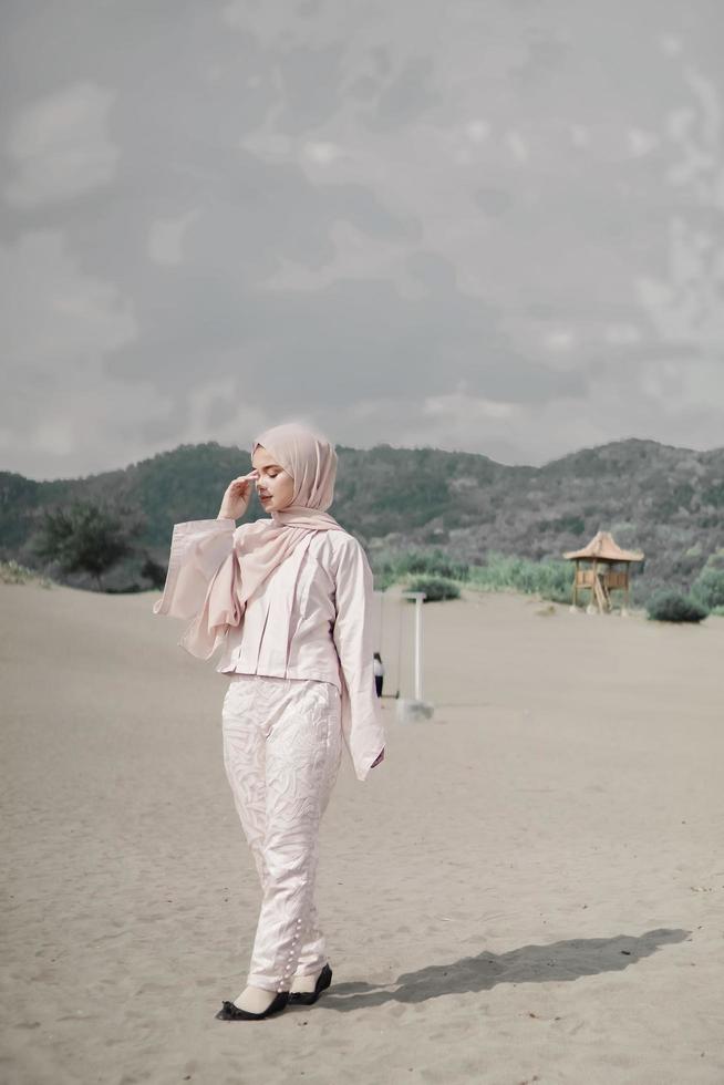 linda modelo feminina islâmica vestindo moda hijab, um vestido de noiva moderno para mulher muçulmana caminha pela areia e pelo mar. um modelo de menina asiática usando hijab se divertindo na praia. foto pré-casamento