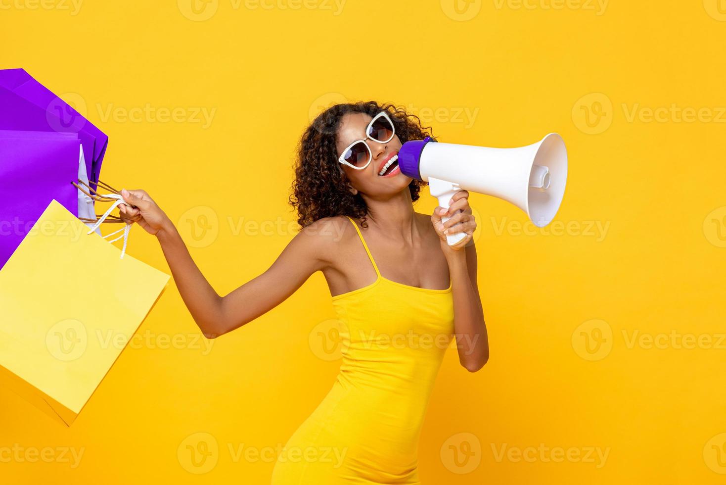 mulher bonita feliz com sacolas de compras e megafone em fundo amarelo colorido isolado para conceitos de venda e desconto foto