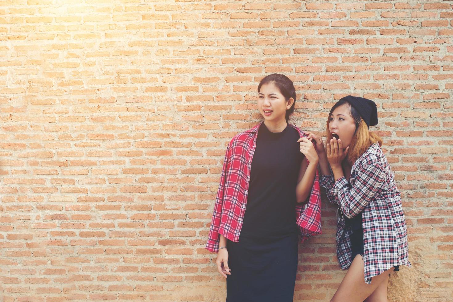 feche o retrato de duas namoradas bonitas e hipster sorriem, divirta-se contra a parede de tijolos urbanos. foto