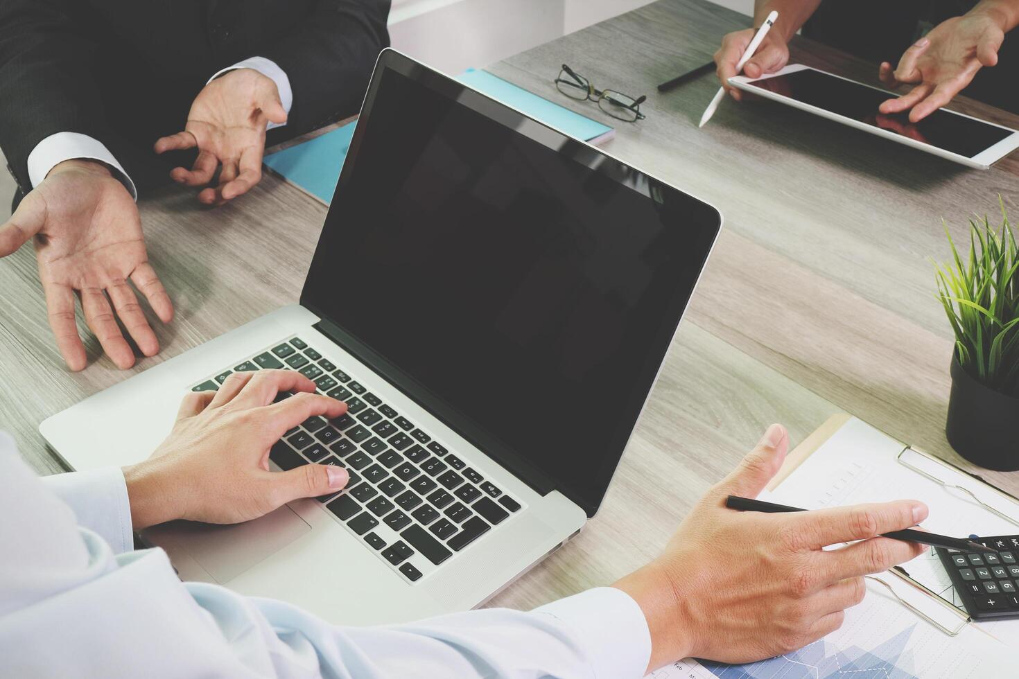 documentos de negócios na mesa de escritório com telefone inteligente e computador portátil de tela em branco e diagrama de negócios gráfico e três colegas discutindo dados em segundo plano foto