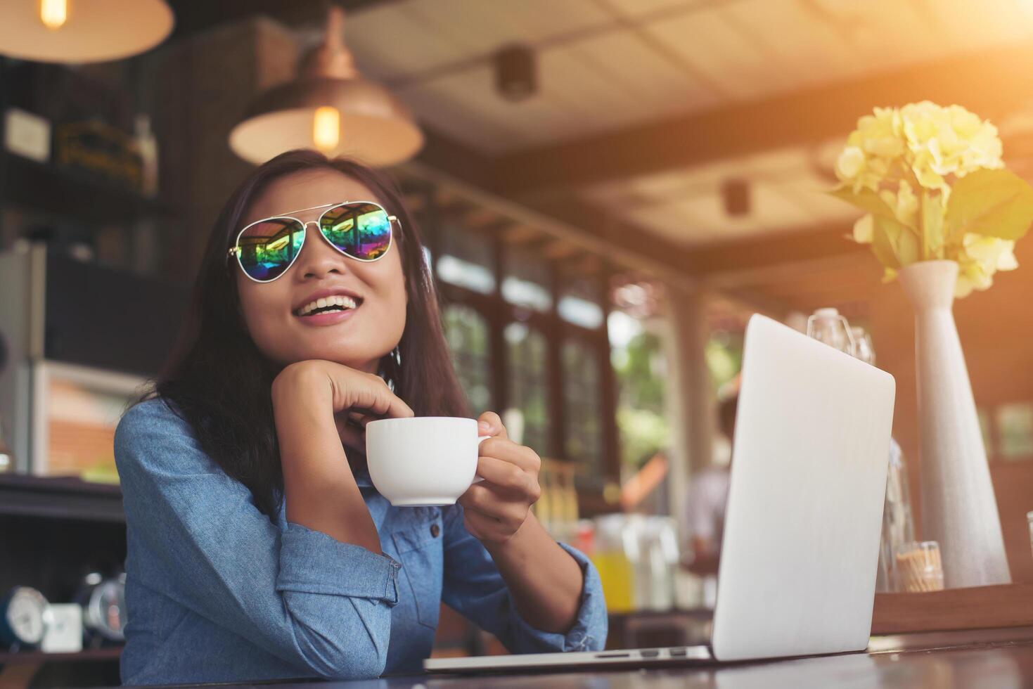 mulher muito jovem hippie sentado em um café com seu laptop, desviou o olhar e sorriu feliz, relaxante com férias, conceito de estilo de vida de mulher. foto