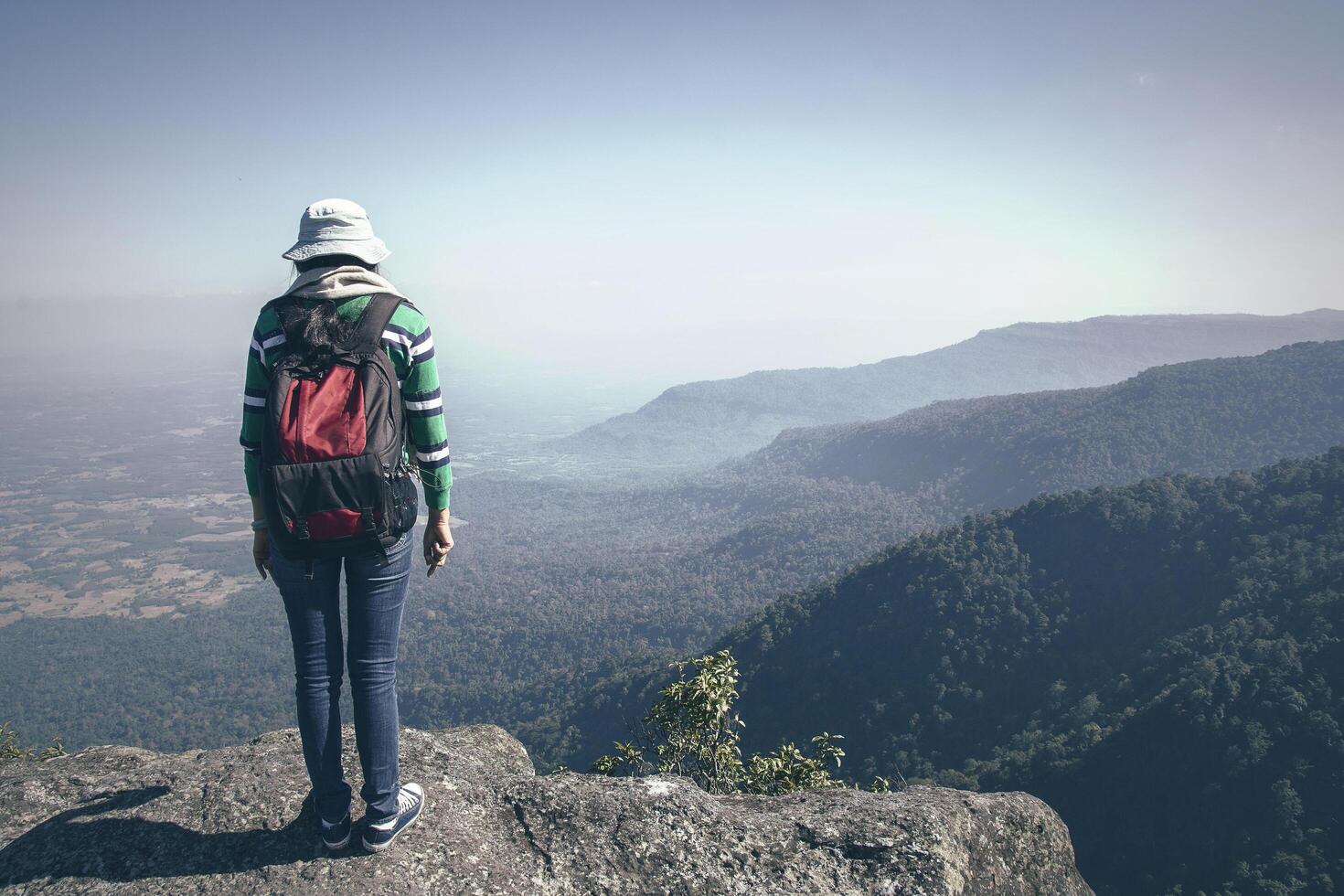 turista jovem com mochila em pé vale vista do topo de uma montanha foto