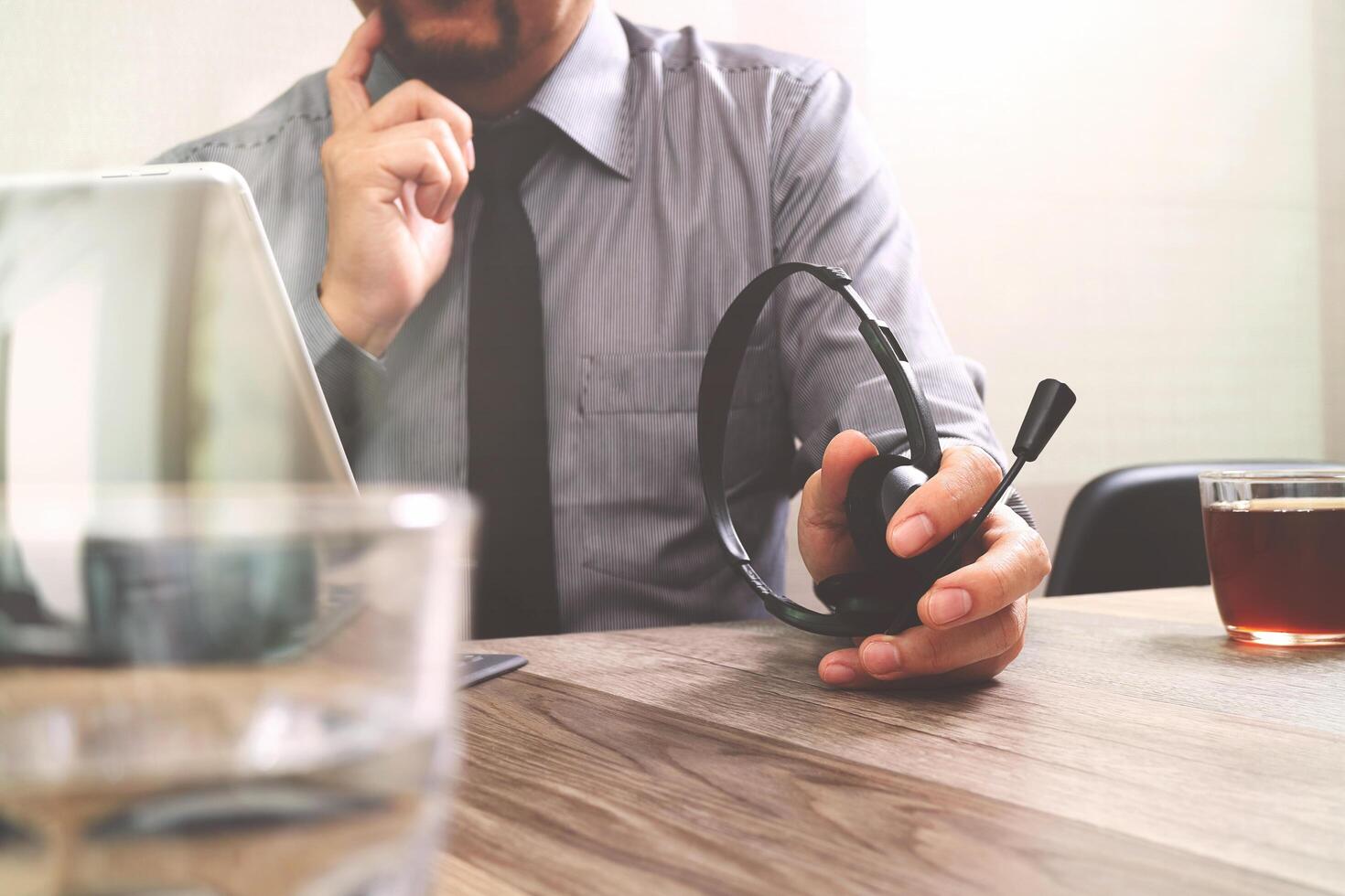 homem de negócios usando fone de ouvido voip com teclado inteligente de encaixe de computador tablet digital, comunicação de conceito, suporte, na mesa de madeira foto