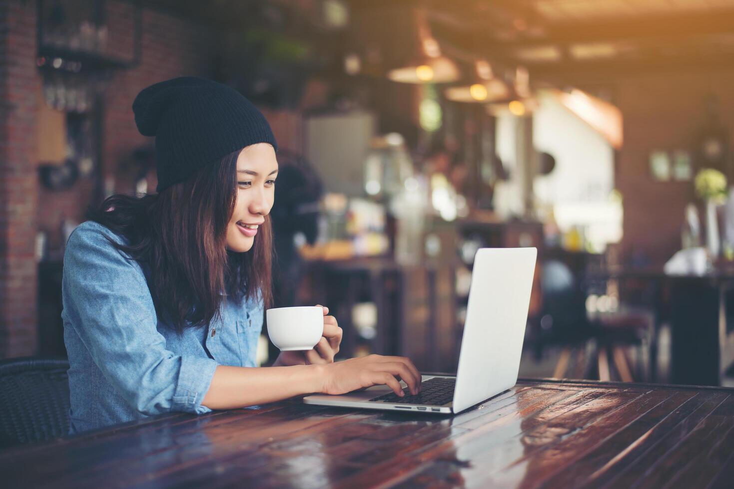 bela jovem hipster sentada em uma cafeteria, relaxe e brinque com seu laptop, encontre informações sobre tempo livre, feliz e divertido. conceito de estilo de vida. foto