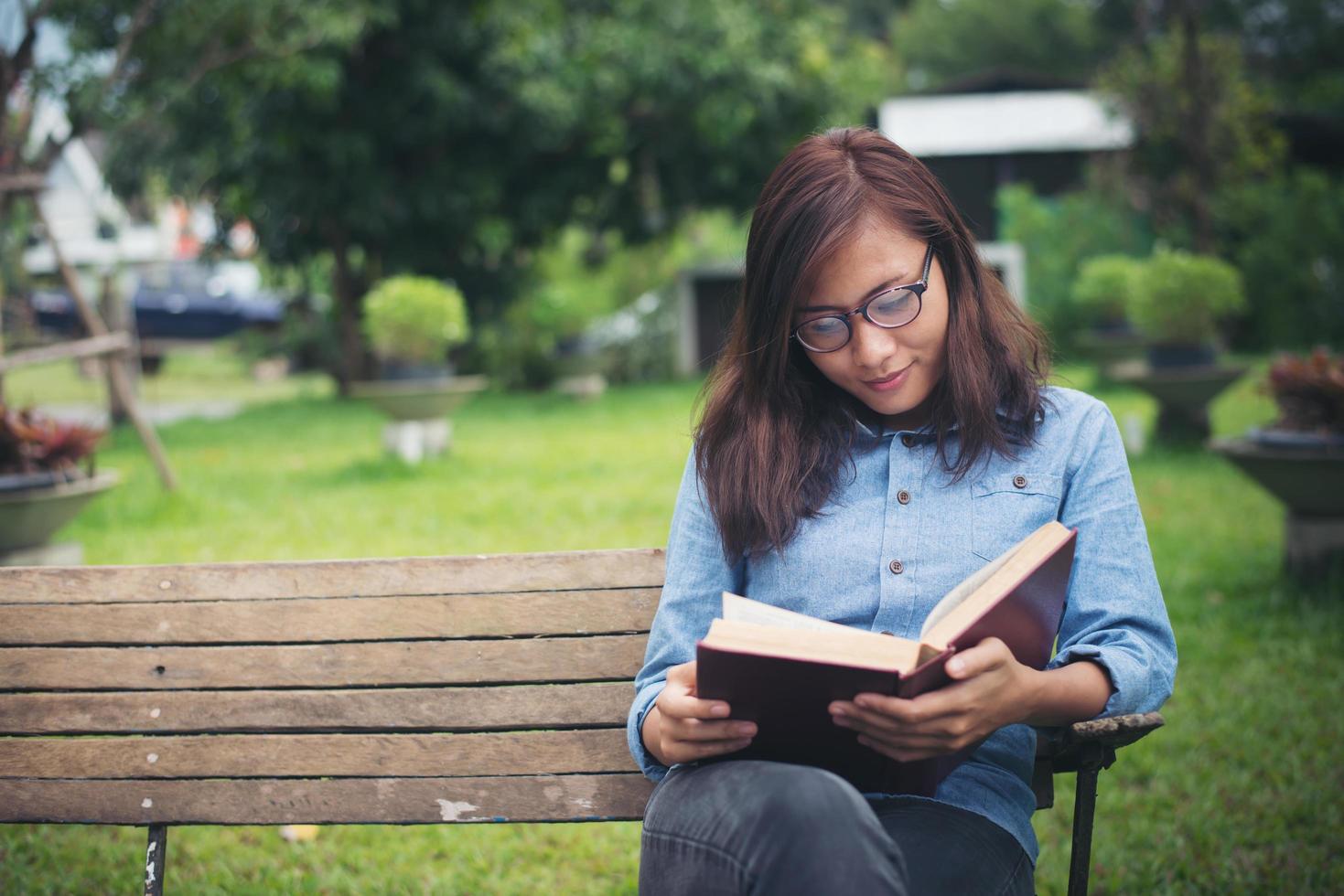 garota encantadora hipster relaxando no parque enquanto lê o livro, aprecia a natureza ao redor. foto