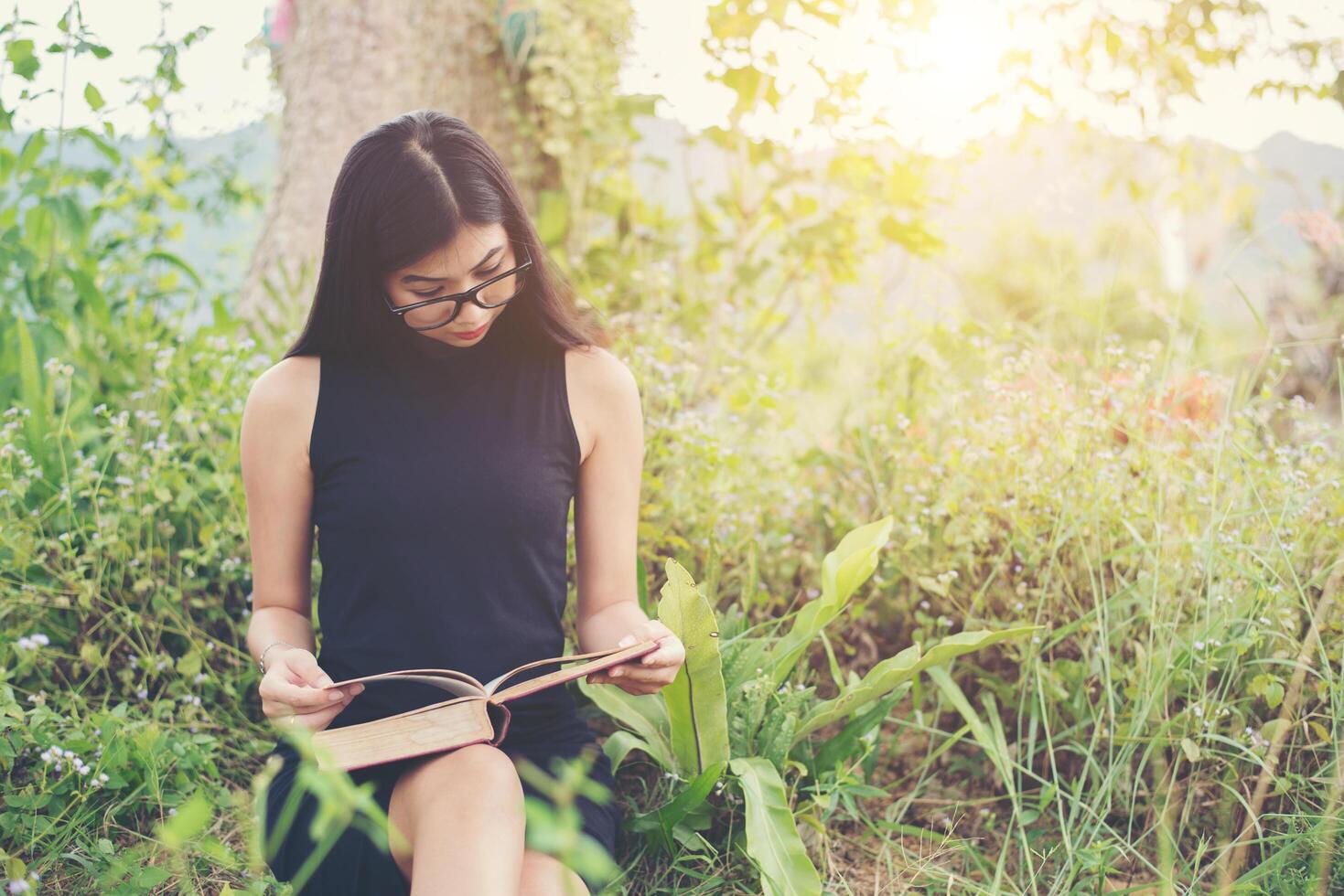 relaxada bela jovem lendo um livro no gramado com sol brilhando. foto