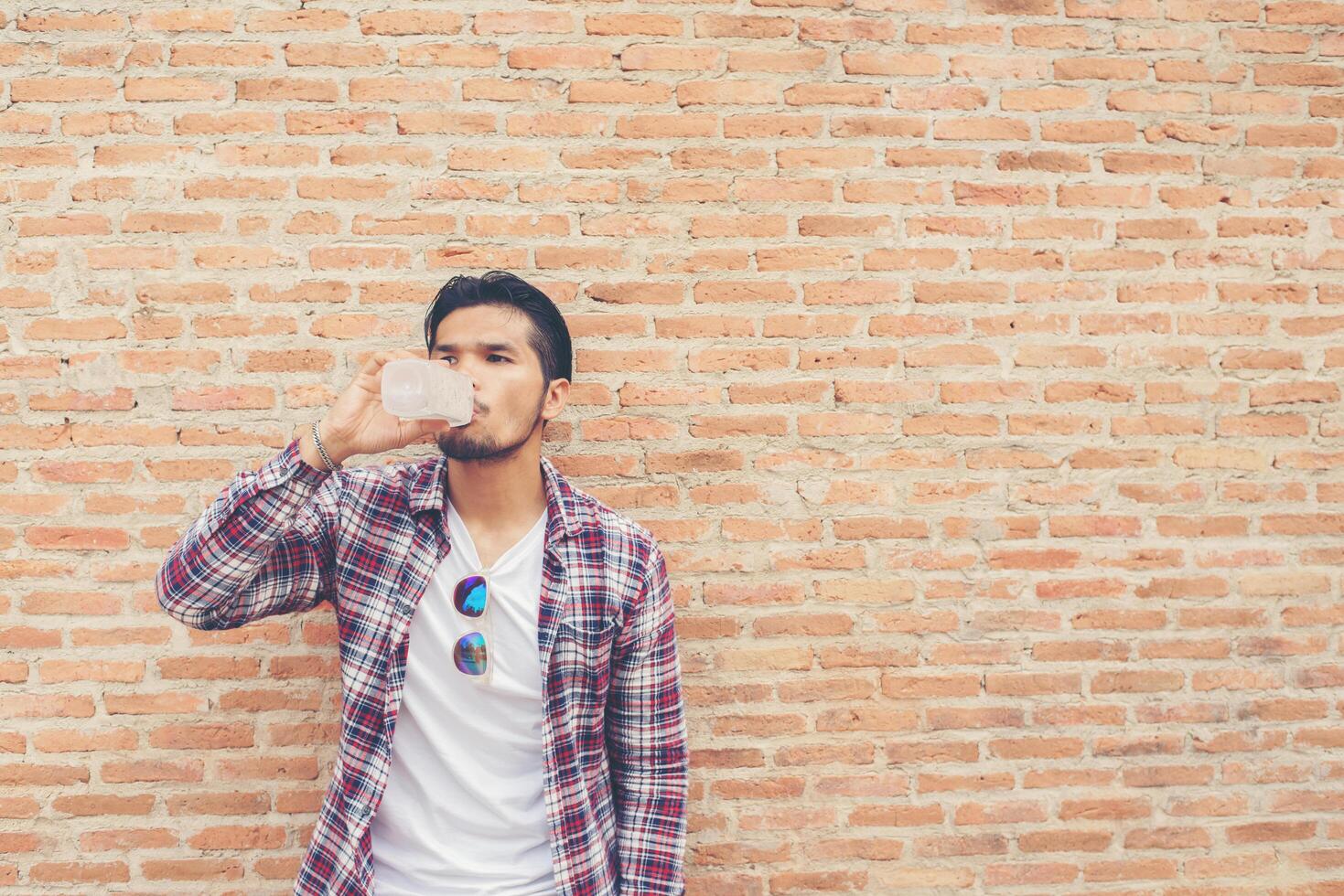 homem barbudo jovem hippie com garrafa de água na camisa xadrez na frente do meio urbano. foto