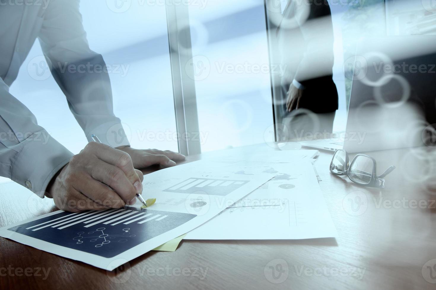 documentos de negócios na mesa de escritório com telefone inteligente e tablet e laptop digital e dois colegas discutindo dados em segundo plano foto