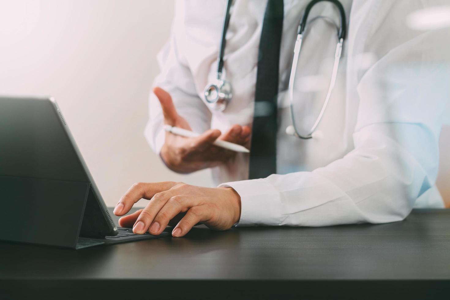 close-up de médico inteligente trabalhando com computador tablet digital e caneta stylus e estetoscópio na mesa de madeira escura foto