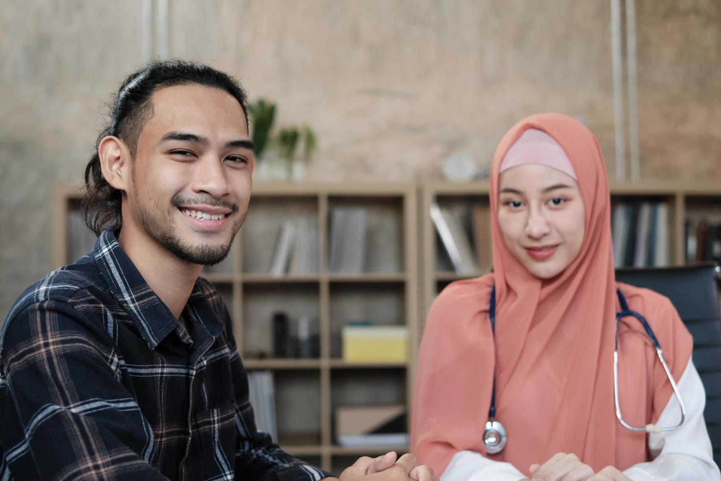 retrato de um homem de pessoa saudável que consulta médica visita após exame com uma jovem médica, bela muçulmana de uniforme com um estetoscópio. um sorriso feliz e olhando para a câmera. foto