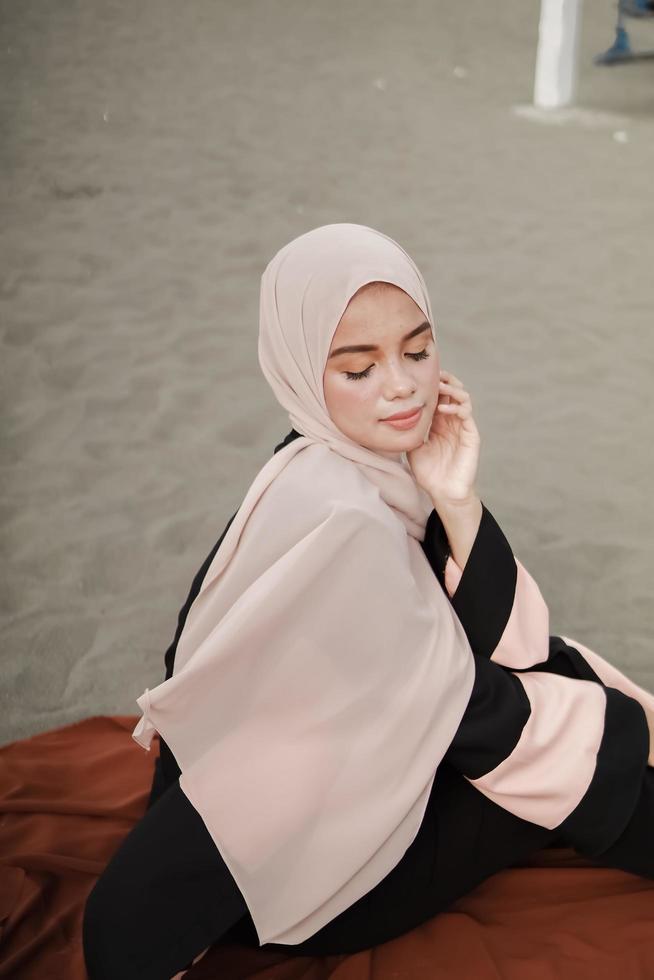 linda modelo feminina islâmica vestindo moda hijab, um vestido de noiva moderno para mulher muçulmana sentada na areia e na praia. retrato um modelo de menina asiática usando hijab se divertindo na praia com árvores foto