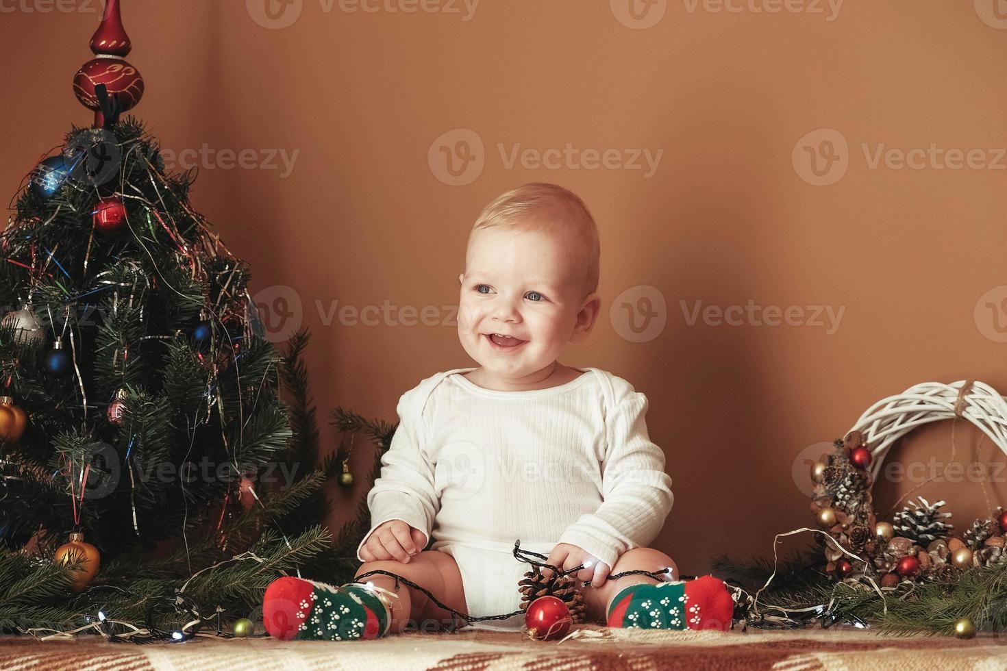 lindo bebezinho comemorando o natal. criança engraçada vestindo um terno de natal perto da árvore de natal no quarto foto