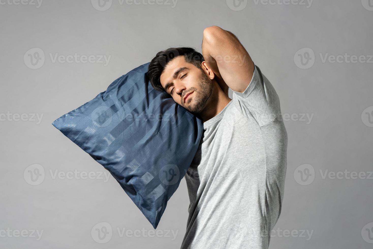 jovem dormindo segurando seu travesseiro em pé no fundo do estúdio isolado cinza claro, conceito de sonambulismo foto