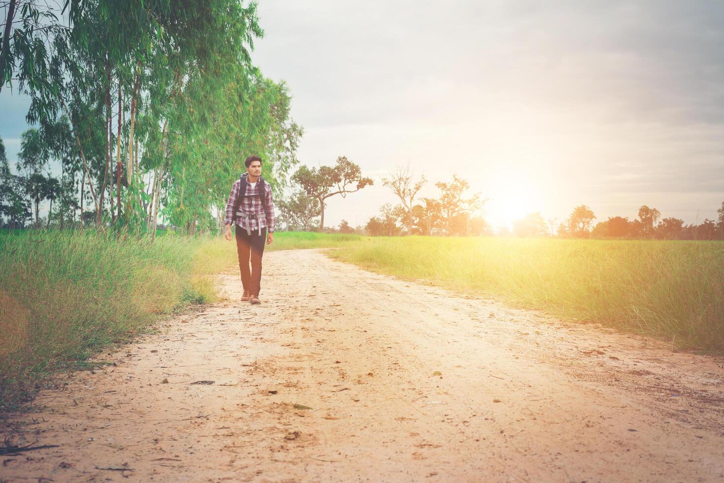 homem jovem hippie com mochila no ombro andando pela zona rural. foto