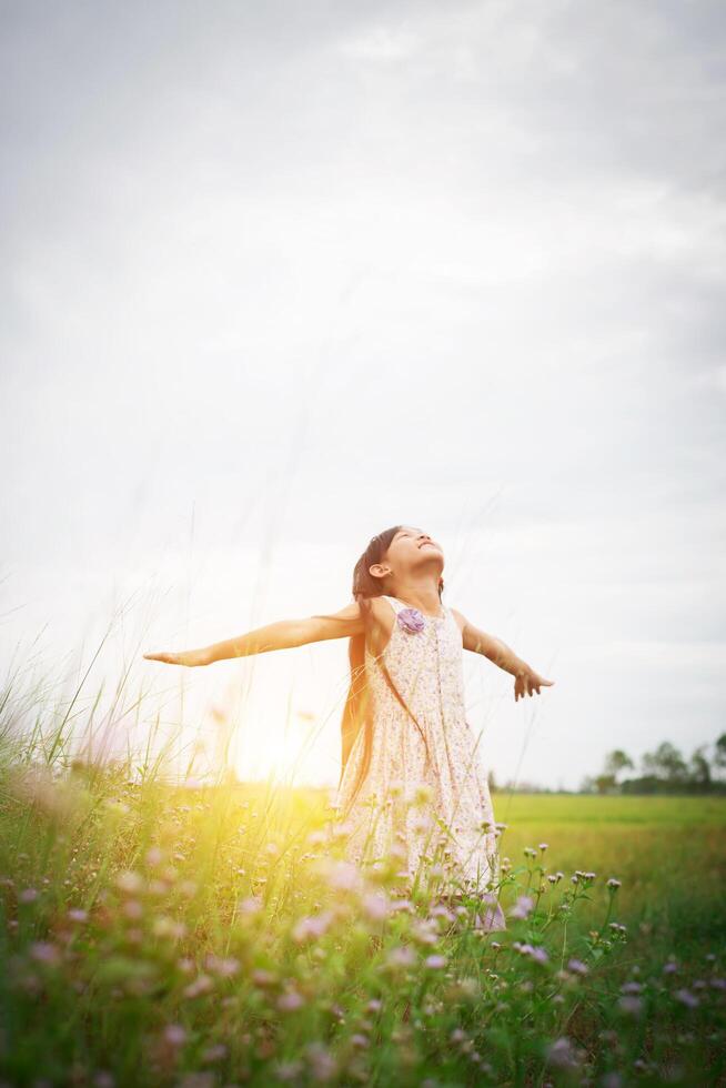 menina asiática bonitinha de pé entre o dia de sol do campo de flores roxas. liberdade desfrutando com a natureza. foto