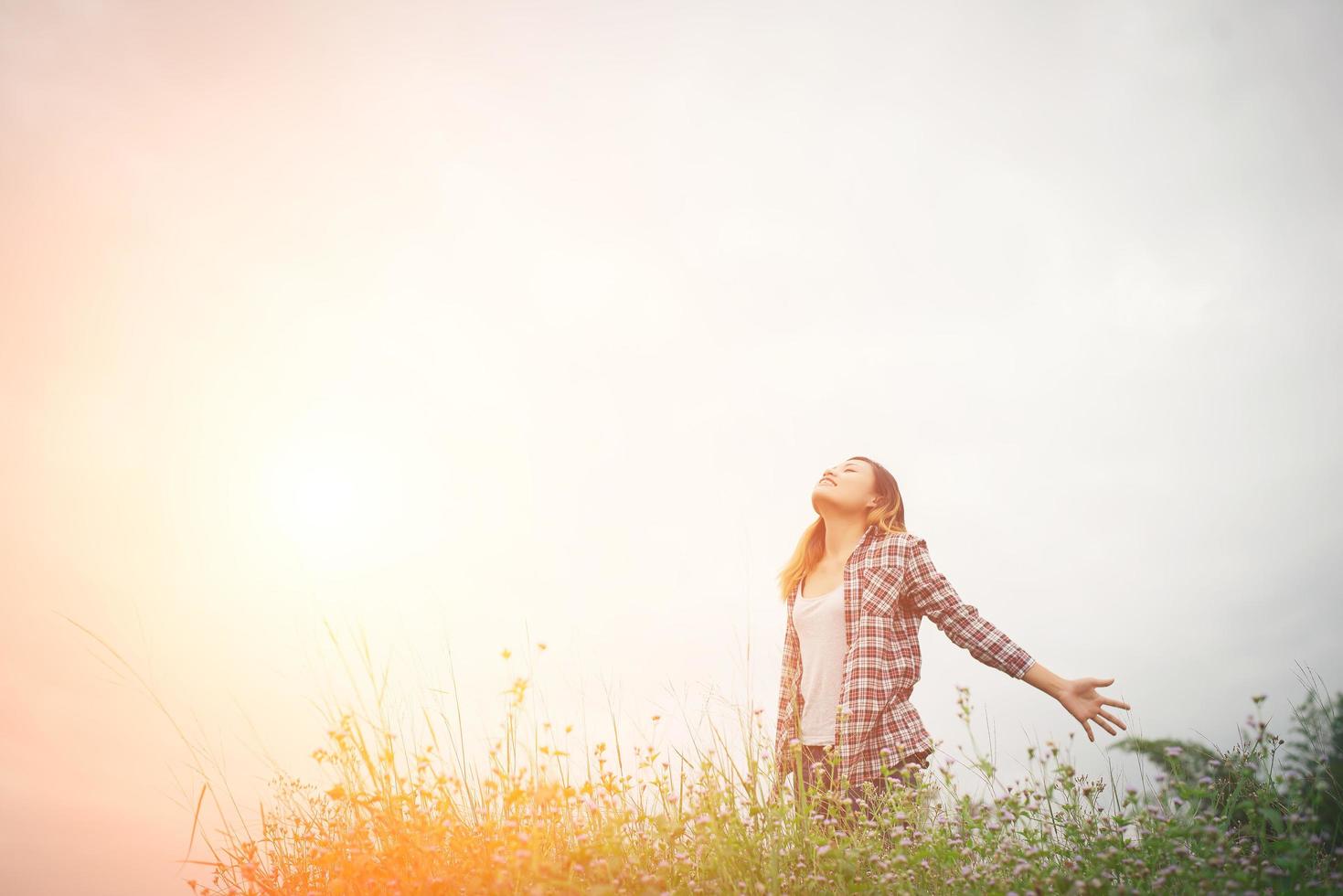 mulher jovem e bonita hipster em um campo de flores ao pôr do sol. liberdade desfrutando com a natureza. foto