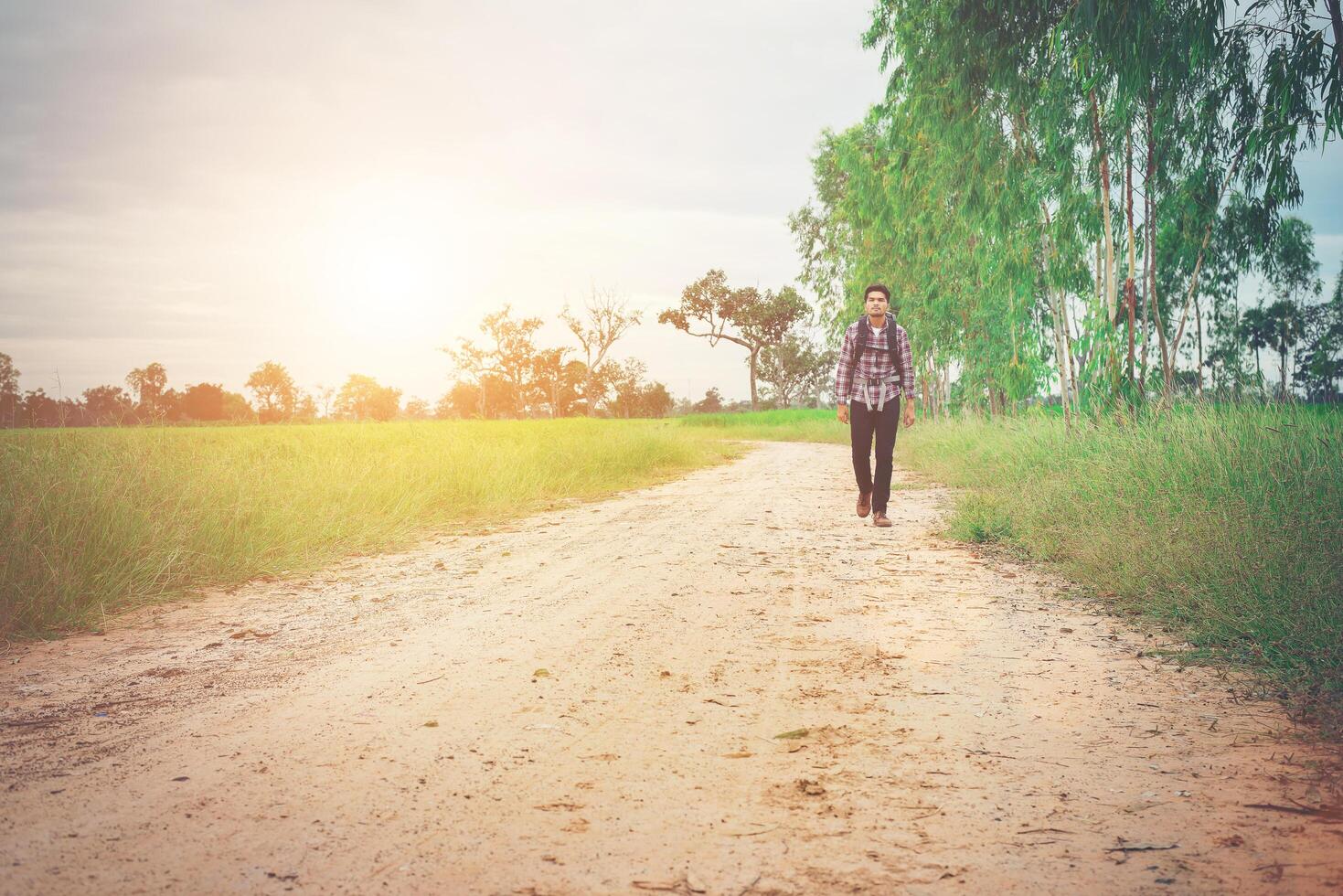 homem jovem hippie com mochila no ombro andando pela zona rural. foto