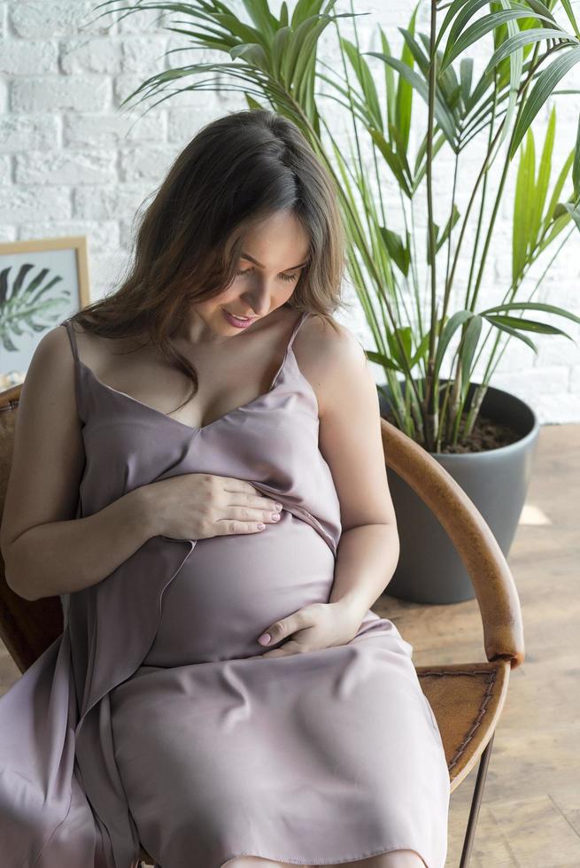 menina grávida sentada em uma cadeira em um fundo branco. foto