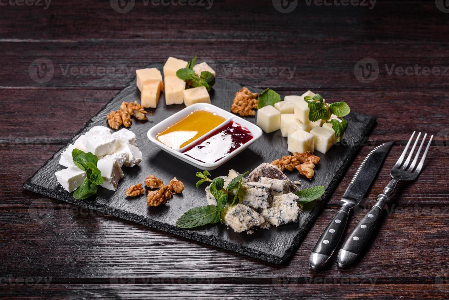 vários tipos de queijo em uma bandeja de xisto com molhos de menta e doces foto