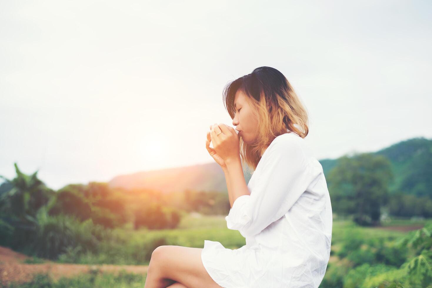 mulher jovem e bonita segurando uma xícara de café sentado no banco uma brisa fresca de manhã. foto