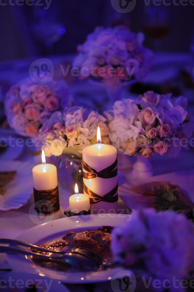 linda mesa decorada com enfeites de flores e velas vermelhas. noite de natal ou decoração de festa de casamento. foto