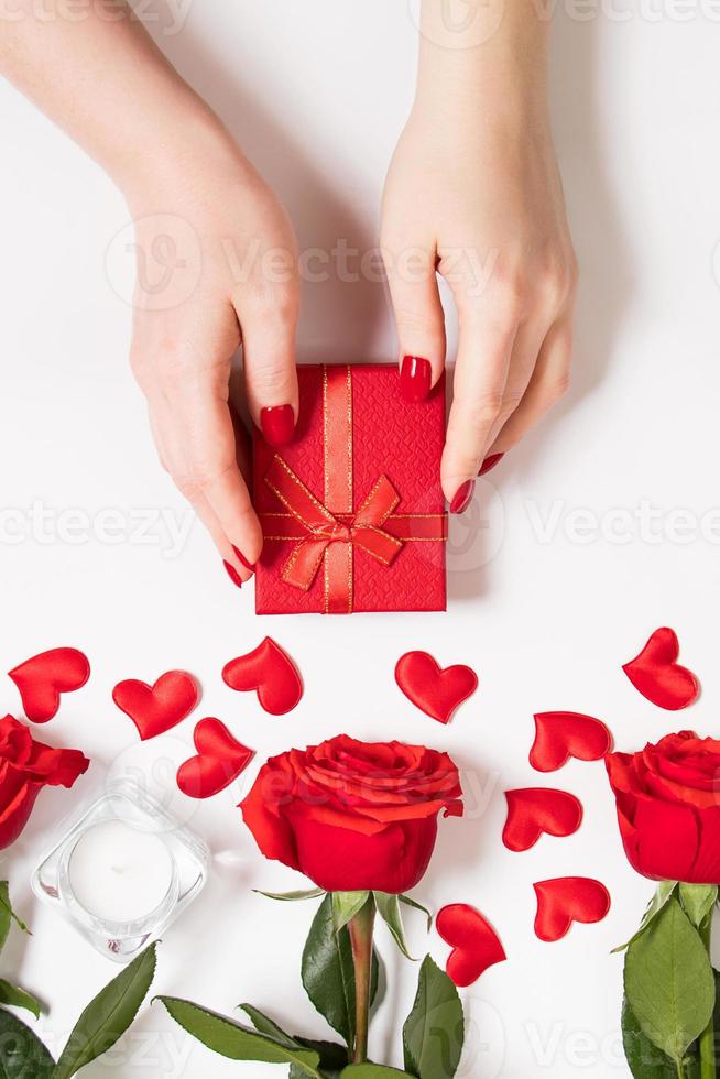 mãos femininas seguram uma caixa de presente para o dia dos namorados. rosas vermelhas e velas em um fundo branco. foto