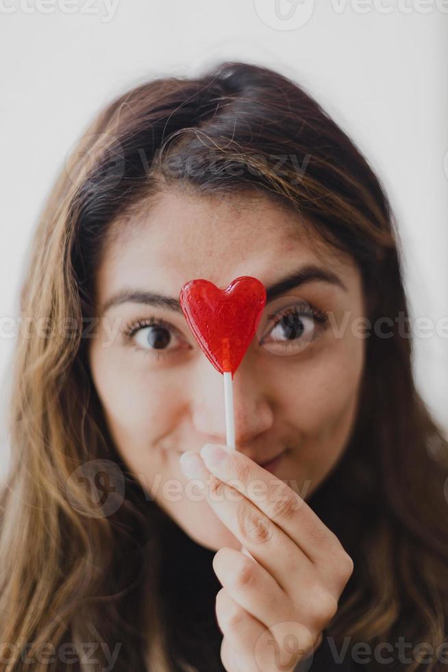 mulher latina apaixonada por um pirulito na mão em forma de coração. Dia dos namorados foto