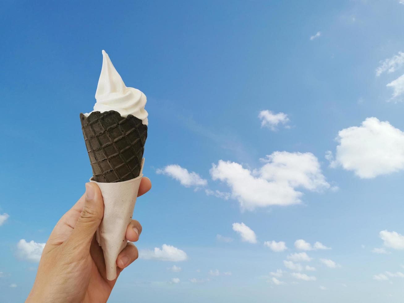 delicioso sorvete no cone de waffle na mão feminina com fundo de céu azul para a temporada de verão. conceito de verão e férias. foto