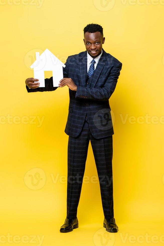 jovem empresário africano como agente imobiliário segurando modelo de recorte de casa em fundo amarelo estúdio isolado foto