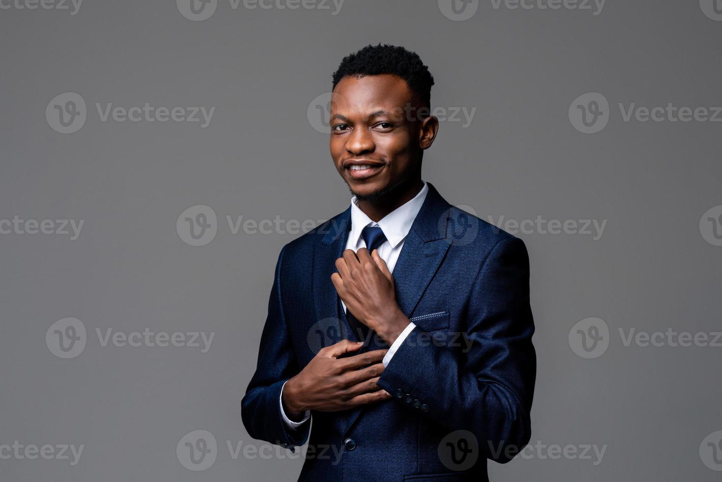 retrato de jovem africano bonito vestindo terno formal segurando a gravata e olhando para câmera isolada no fundo cinza do estúdio foto