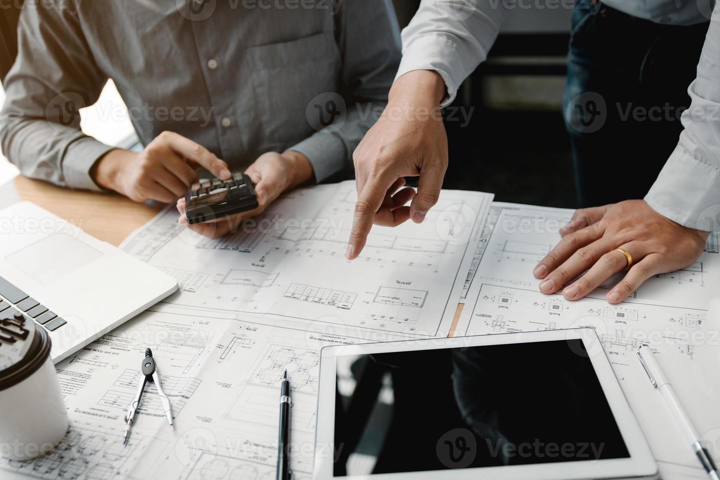 dois engenheiros trabalhando juntos e usando tablet digital procurando planta e análise com plano arquitetônico na mesa. foto