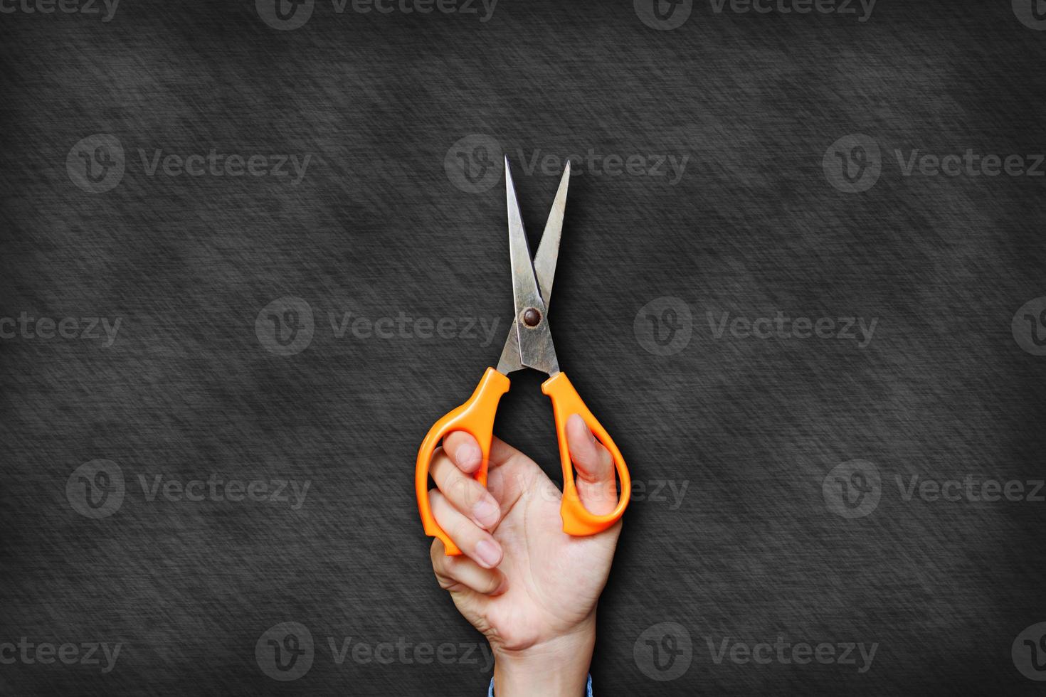 mão está segurando uma tesoura laranja no fundo do quadro-negro. foto