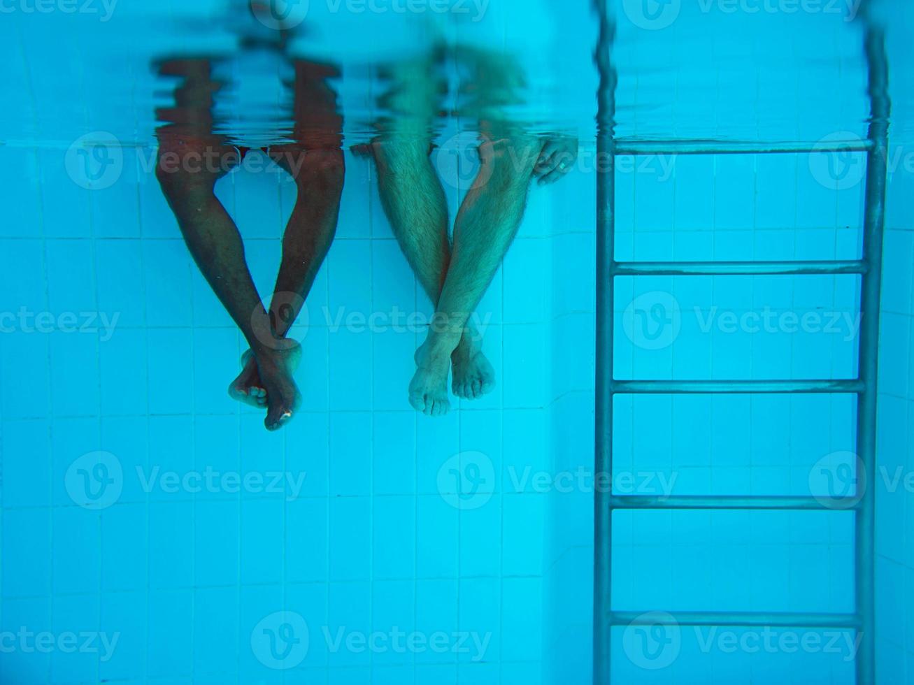 as pernas do homem afro-americano adulto e as pernas da mulher caucasiana debaixo d'água na piscina. conceito de esporte, recreação, férias e amizade foto